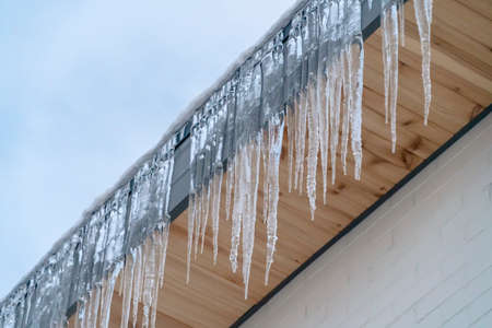 Sharp icicles on the eaves of a roof in Utah. Sharp translucent icicles hanging on the eaves of a...
