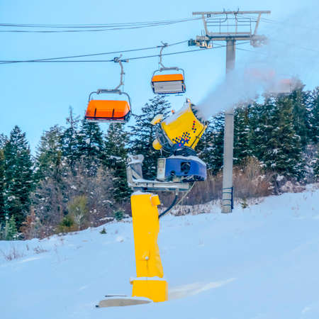 Snow cannon and ski lifts on ski resort in Utah. Snow cannon spraying artificial snow on a ski...