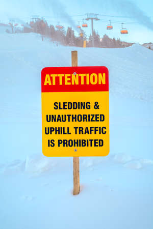 Attention sign against snow at a ski resort. Sign that reads Attention Sledding and Unauthorized...