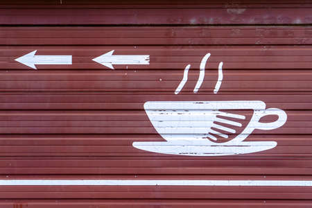Coffee This Way illustration sign on brown surface. Cup of coffee icon and arrows pointing to the direction of a coffee shop. The sign is painted on a brown corrugated metal surface.の写真素材