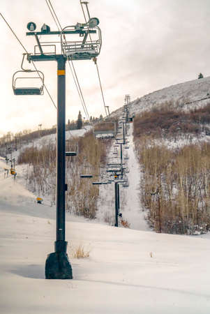 Frosty ski lifts and snow cannons in Park City. Frosty ski lifts in Park City over snow covered mountain on a cloudy day. Yellow snow cannons can be seen making artificial snow on the ski resort.の写真素材