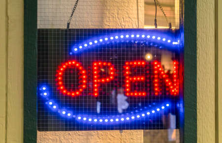 Neon Open sign on the door of an establishment. Close up of a red and blue neon Open sign hanging on the door of an establishment with screen mesh wire behind the glass surface.の写真素材
