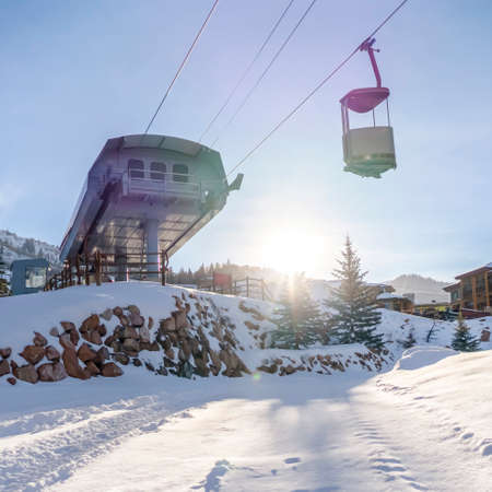 Ski lift over snow against mountain and bright sun. Ski lift over the sunlit snow covered mountain in Park City, Utah. Vast sky and bright sun behind a snowy mountain can be seen in the background.の写真素材