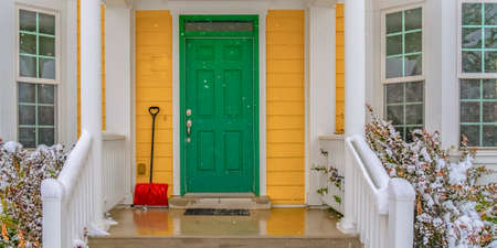 Snow showel beside the green front door of a home. Red snow shovel leaning on the yellow wall beside the green front door of a home. The stairs is wet because of snow during winter in Daybreak, Utah.の写真素材
