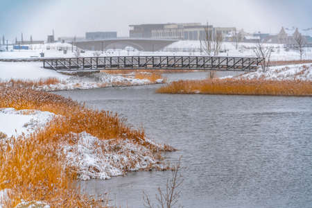 Scenic view of Oquirrh Lake in winter. Scenic view of Oquirrh Lake in Daybreak, Utah on a frosty winter day. Buildings and sky can be seen beyond the bridges crossing over the lake with snowy shore.の写真素材