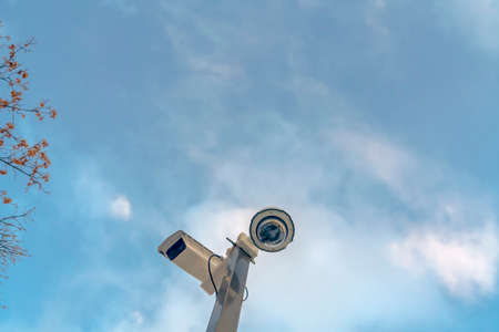 Security cameras against cloudy blue sky and tree. Looking up at security cameras on an area under...