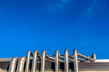 Metal pipes of a building against vivid blue sky. Metal pipes on the exterior wall of a building against a vivid blue sky. The shiny metal pipes on the wall and roof are illuminated by sunlight.の写真素材