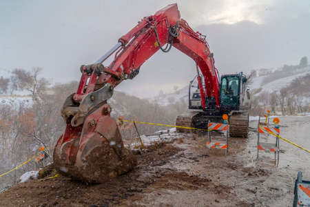 Excavator on a muddy road with barricades and yellow tape viewed in winter