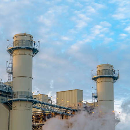Square Cloudy blue sky viewed behind the towers and buildings of a Power Plant