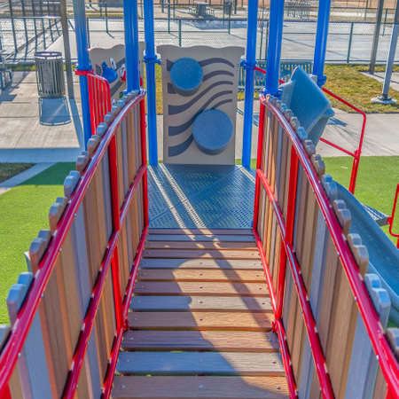 Clear Square Playground equipment with a bridge and slide against vibrant green lawn. Picnic table and benches can be seen near the area on this sunny day.の写真素材