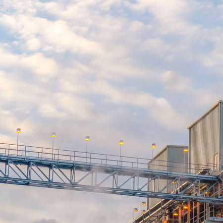 Square Steam emitted from a Power Plant in Utah Valley against cloudy blue sky. A walkway lined with...