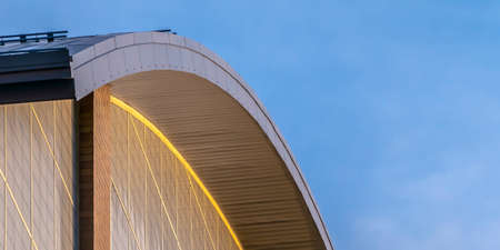 Close up view of the exterior of a building with a curve shaped roof. A blue sky with thin clouds can be seen in the background on this sunny day.の写真素材