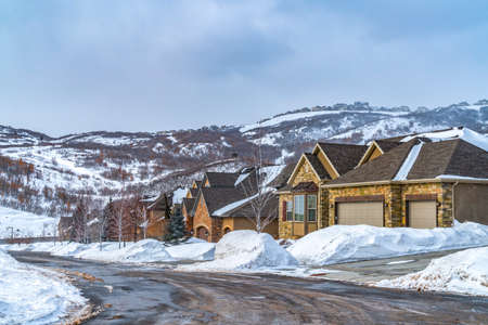 Road winding through a snow covered landscape with lovely homes in winter. A distant snowy mountain...