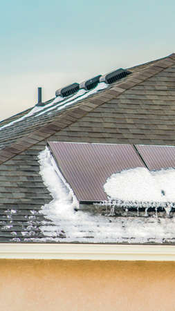 Clear Vertical Roof of a home with solar panels against a vast cloudy blue sky. Powdery white snow...