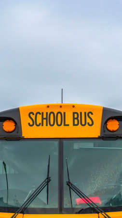 Vertical Front view of a yellow school bus with homes and cloudy sky in the background. Several side...