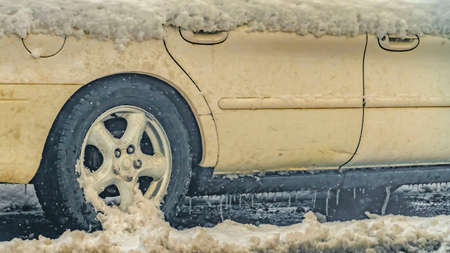 Panorama White car covered with snow on a frosty and wet road in Daybreak Utah. Icicles formed at...