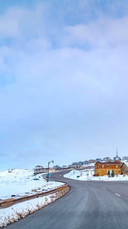 Clear Vertical Paved road curving through a mountain blanketed with snow in winter. Lovely homes at...