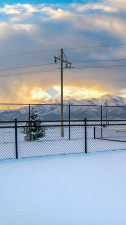 Vertical Tennis courts on a landscape blanketed with snow during winter season. A stunning snow capped mountain against cloudy sky at sunset can be seen in the distance.の写真素材