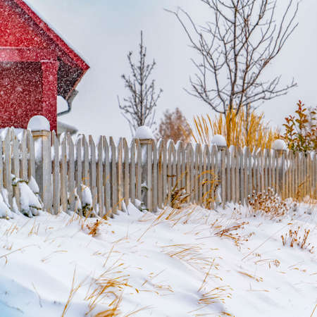 Clear Square Winter landscape with vibrant red home and snow topped picket fence in Daybreak. Snow is falling from the cloudy sky blanketing the Utah Valley terrain.の写真素材