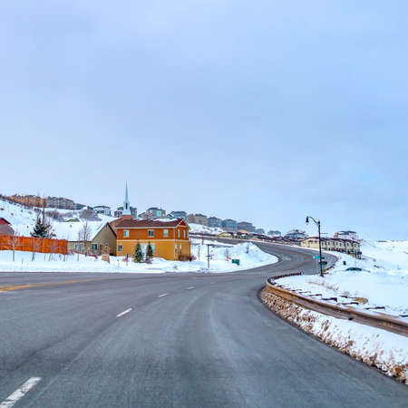 Clear Square Paved road curving through a mountain blanketed with snow in winter. Lovely homes at the side of the road can also be seen aganst the cloud filled sky.の写真素材