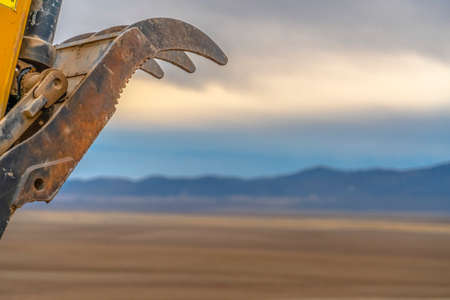 Excavator bucket teeth against silhouetted mountain and cloudy sky background. The bucket teeth of the yellow construction machinery is covered with rust.の写真素材