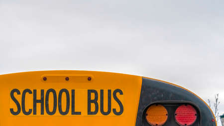 Clear Panorama Close up of the back side of a yellow school bus against homes and cloudy sky. The...