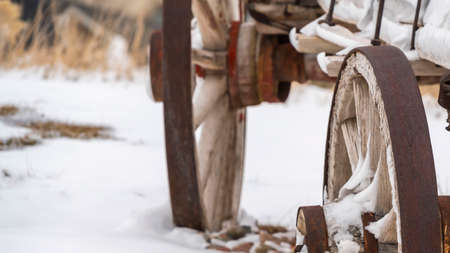 Clear Panorama Close up of the rusty wheels of an old wooden wagon viewed in winter. The wagon and the rocky terrain is blanketed with powdery white snow.の写真素材