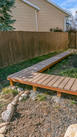 Clear Vertical Wooden walkway inside the yard of a home viewed on a sunny day. The walkway is...