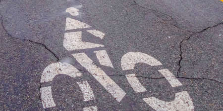 Panorama Bicycle lane sign painted on a road with cracks. Close up of a weathered road with a white...
