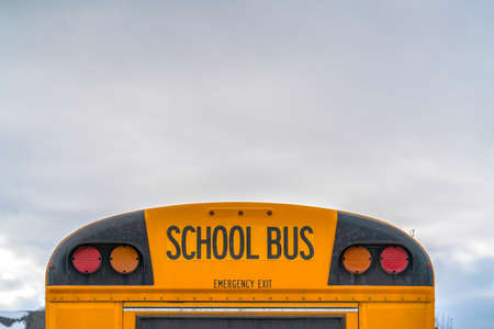 Rear of a yellow school bus with signal lights and emergency exit window. A sky filled with clouds and snowy landscape in winter can be seen in the background.の写真素材
