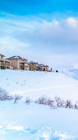 Vertical Panoramic view of a stunning snowy mountain against vibrant sky with clouds. Houses built on top of the frosty slope can be seen in the distance.の写真素材