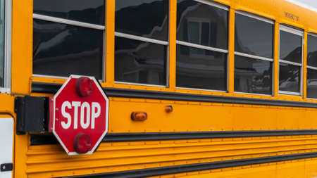 Clear Panorama Side view of a school bus on a road passing through snowy homes in winter. Reflective windows and stop sign with signal lights can be seen at the exterior of the bus.の写真素材