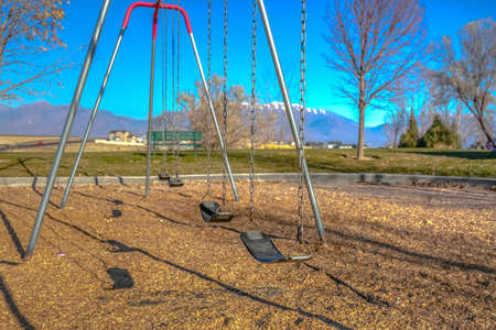 Swings at a playground casting shadows on the ground on a sunny dayの写真素材