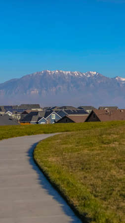 Vertical frame Paved road on a lush grassy hill overlooking beautiful houses on a sunny dayの写真素材
