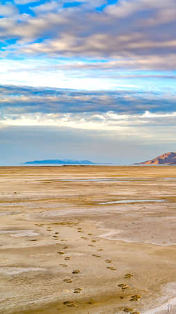 Vertical Sandy shore of a lake and distant rugged mountain under cloudy blue sky