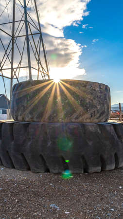 Vertical frame Sun in the cloudy blue sky shining brightly behind a pile of old rubber tiresの写真素材