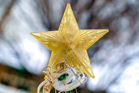 Yellow star Christmas decor isolated against a blurry background of tree and sky