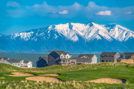 Grassy hill with houses overlooking a vast lake and snow capped mountainの写真素材