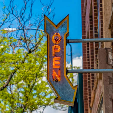 Square Open arrow sign on a building with vibrant trees and blue sky in the backgroundの写真素材