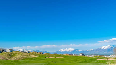 Panorama Vast grassy field with a curving paved road and houses beyond the slopesの写真素材