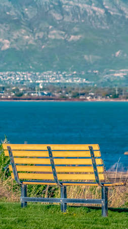 Panorama frame Close up of a bench facing a lake with glistening blue water on a sunny dayの写真素材