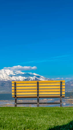 Panorama frame The back of a bench overlooking a lake and snowy mountain on a sunny dayの写真素材