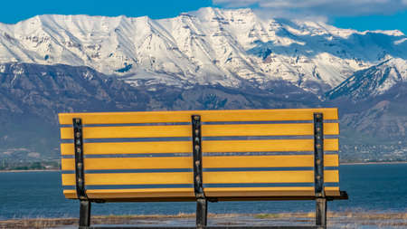 Panorama Back view of an empty bench overlooking a calm lake on a sunny dayの写真素材