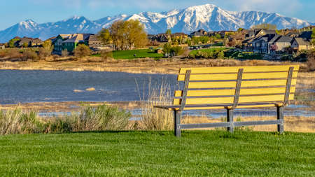 Panorama Bench on a grassy field overlooking lake and snowy mountain against blue skyの写真素材