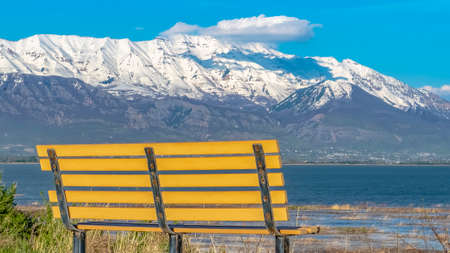 Panorama frame Empty bench with view of snow capped mountain towering over lake and valleyの写真素材