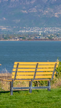 Panorama frame Close up of a bench on a grassy terrain ovelooking a lake on a sunny dayの写真素材