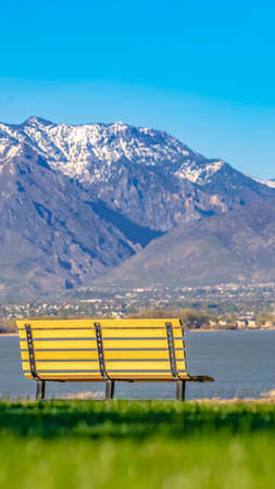 Panorama frame Empty bench facing an amazing view of a lake and mountain capped with snowの写真素材
