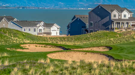 Panorama frame Grassy hill with houses overlooking a vast lake and snow capped mountain
