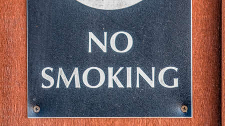 Panorama frame Close up of a No Smoking sign screwed to a reddish brown wood surfaceの写真素材