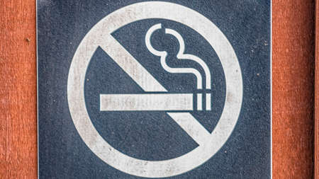 Panorama Close up of a No Smoking sign screwed to a reddish brown wood surfaceの写真素材